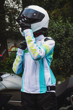 Person wearing a white and blue motorcycle jacket with gloves and helmet, standing next to a motorcycle.